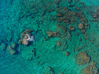 Aerial view of crystal clear turquoise water with rocks and coral formations beneath the surface.