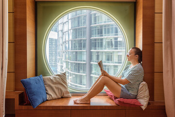 Woman seating near a round window and reading a book