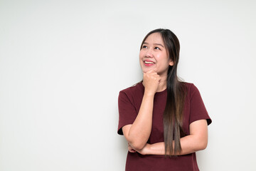Studio portrait of young Asian woman thinking and smiling while looking up holding hand on chin