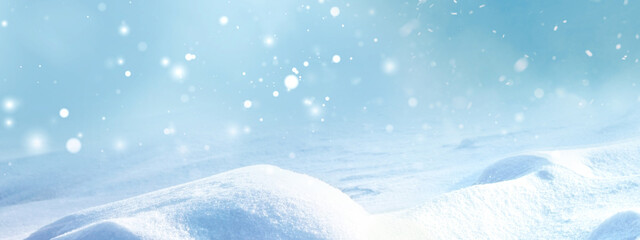 Winter snow background with snowdrifts, with beautiful light and snow flakes on the blue sky, banner format, copy space.