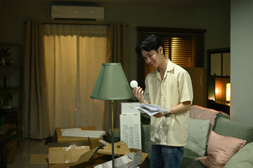 Focused and cheerful, man assembles lamp, checking guide and handling bulb with care in living room at evening