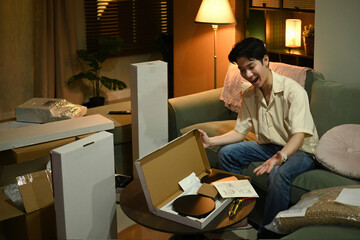 A Young Asian man excitedly opens a furniture kit, getting ready to build and decorate his space