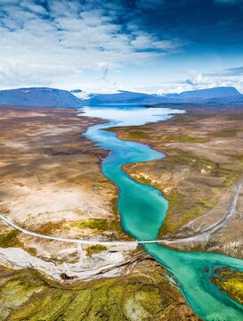Aerial view of glacial river carves through rugged terrain, contrasting with the distant blue mountains and vast open landscapes, Hvita, Bl&Atilde;&iexcl;sk&Atilde;&sup3;gabygg&Atilde;&deg;, Iceland.