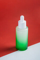 Green glass cosmetic bottle, Skin care or sunscreen cosmetic with stylish props on red background.