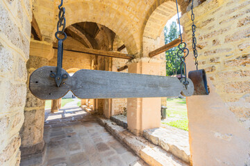 An old, weathered wooden talanton hangs from two metal chains in the stone archway of a historic...