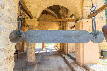 An old, weathered wooden talanton hangs from two metal chains in the stone archway of a historic...