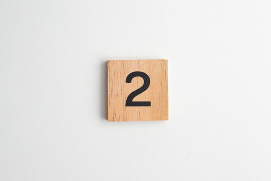 Single wooden block with the number "2" printed in black on a white isolated background. Educational toy for children learning numbers or for creative design and math concepts.