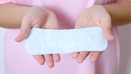 Woman wearing pink dress displaying sanitary pad, highlighting feminine health product offering comfortable menstrual protection