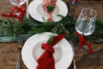 Stylish christmas table setting with modern plate, red and green napkins, cutlery, glass, fir...