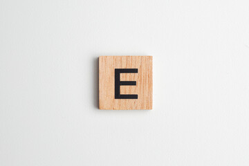 Wooden alphabet block with the letter "E" on a white isolated background, flatlay style with copy space. Educational wooden toy for children or creative design projects.