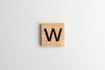 Wooden alphabet block with the letter "W" on a white isolated background, flatlay style with copy space. Educational wooden toy for children or creative design projects.
