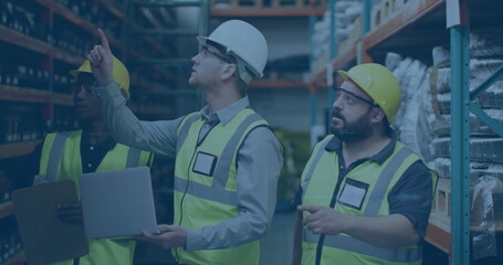 Reviewing workers wearing helmets checking stock in warehouse aisle, with laptop and clipboard