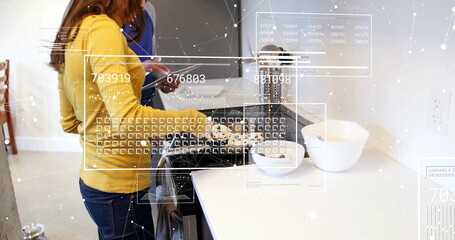 Cooking couple using gas stove in modern kitchen, woman frying food and man reading tablet