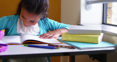 Leaning student in turquoise cardigan writing in open notebook at study nook by window, copy space