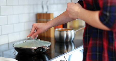 Cooking man wearing plaid shirt lifting frying pan lid on kitchen stove with saucepan, copy space