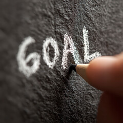 Goal written on blackboard with chalk and hand holding chalk close up, symbolizing business goal setting and marketing strategy