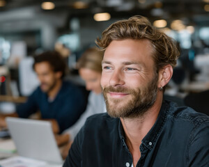 Smiling man bearded man casual shirt office environment coworking space business professionals teamwork collaboration modern workplace laptop focused creative young adult positive expression male