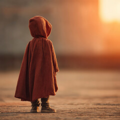 Child in brown hooded cape standing on textured ground at sunset with warm light creating peaceful and contemplative mood