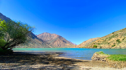 Vacation on the shore of the beautiful mountain lake Iskanderkul. A beautiful pond with ridges, hills and rocks in the background