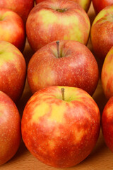 A close-up vertical shot shows a group of fresh, red and yellow apples arranged closely together on a wooden surface