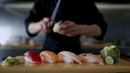 Asian man chef preparing sushi and slicing fish on a wooden board at a gourmet kitchen counter, close up footage.
