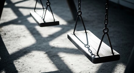 Two empty swings in a playground casting shadows on the ground