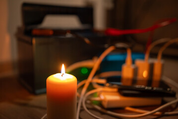A candle as the only source of light during a blackout. A close-up of a lit candle, illuminating a space where gadgets are being charged from a car battery using inverter