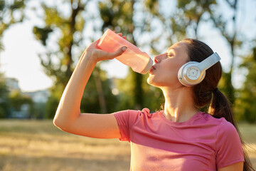 A woman enjoys refreshing hydration from a water bottle after an intense workout session in a park...