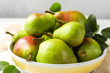 Fresh ripe pears in bowl and green leaves on table, closeup