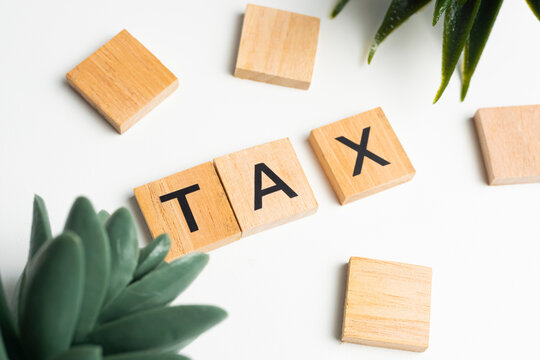 Wooden Scrabble tiles with the letters "TAX" on a white background. The word "TAX" is written on a wooden piece or wooden cube. - Powered by Adobe