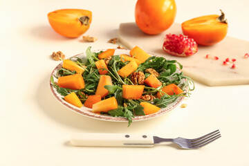 Plate of delicious salad with persimmon and walnut on yellow background
