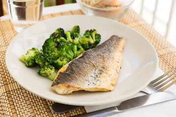fried fillet of sea bass with garnish of broccoli on black warm stone plate