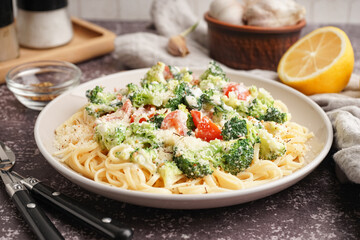 Plate of tasty pasta with broccoli and tomatoes on grunge grey background