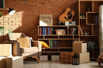 Many various unwanted things and cardboard with text GARAGE SALE near brick wall in room