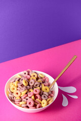 Bowl with colorful sweet cereal rings and paper milk drops on pink table
