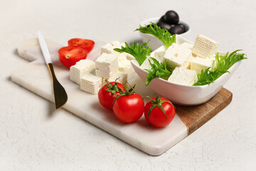 Board with cubes of feta cheese, cherry tomatoes and arugula on white background