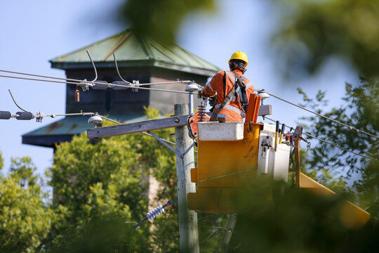 Un &eacute;lectricien travaille sur un poteau &eacute;lectrique avec un marteau-piqueur en arri&egrave;re-plan. Un ouvrier travaille sur des fils &eacute;lectriques. Des ouvriers sur le chantier d'un transformateur haute tension