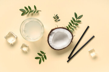 Half of fresh coconut with glass of water, ice cubes and leaves on yellow background