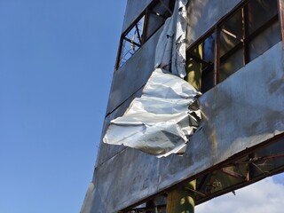 Urban decay: a torn billboard hangs from a weathered, rusted metal structure against a clear blue sky, symbolizing economic hardship and neglect
