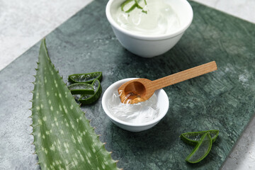 Bowls of aloe vera gel and leaf on grey background
