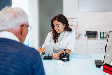 Audiologist is presenting a hearing aid device to a senior patient during a consultation in a...