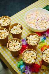 Paper cups with popcorn and bowl of colorful marshmallows on festive table