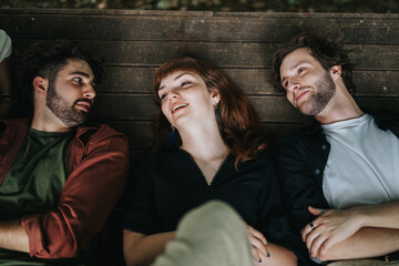 Three close friends sharing a joyful moment while lying on a wooden bench outdoors, enjoying the day.