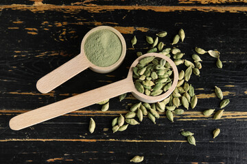 Spoons with cardamom spice and powder on black wooden background