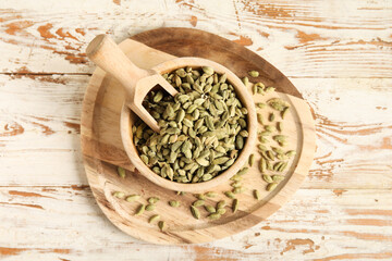 Bowl with cardamom spice and scoop on white wooden background