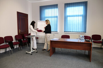 Two women working together in a modern office: signing documents and discussing charts on a flipchart during a work meeting