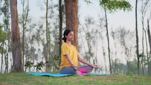 Peaceful young woman meditating in the forest during sunrise.