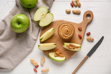 Cutting board with fresh apple slices and bowl of sweet peanut butter on white wooden background