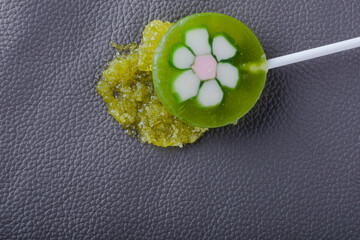  A green sticky lollipop, a dip on the upholstery of a gray leather sofa. Concept of daily stains...