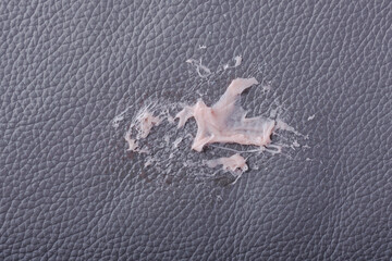 Chewing gum has become stuck on a gray leather textured surface, showing its stretching and gooey...